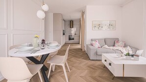 Una sala de estar moderna con un sofá gris, una mesita de centro blanca y un comedor con una mesa redonda y sillas.