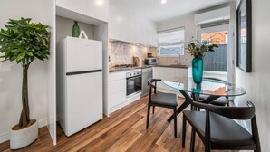 Una cocina moderna con armarios blancos, una mesa de comedor de vidrio y una planta en maceta.