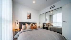 Una habitación de hotel moderna con una cama grande, mesitas de noche, un espejo y un cuadro en la pared.