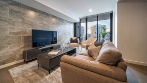 Una sala de estar moderna con un televisor de pantalla plana grande, una mesa de centro oscura, un sofá color beige y dos sillones.