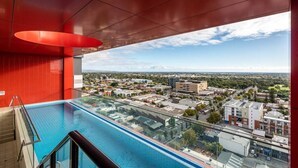 Una piscina interior moderna con vista a la ciudad, paredes rojas y cielo despejado.