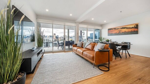 Un salon moderne avec un canapé en cuir, un coin repas et de grandes fenêtres offrant une vue sur la ville.