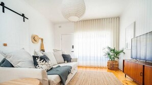 A modern living room with a sofa, a small round table, a TV, and a large window with curtains. - Salt at Arlo`s - Cosy Comfort near Glenelg Beach (Glenelg South)