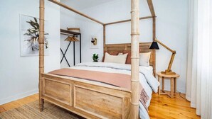 A four-poster bed with a wooden frame and a headboard, a bedside table with a lamp, and a small plant on the nightstand. - Salt at Arlo`s - Cosy Comfort near Glenelg Beach (Glenelg South)