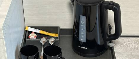 A tray with a black coffee maker, two black mugs, a spoon, a packet of sugar, and a packet of coffee creamer.