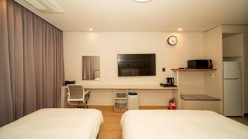 A hotel room with two beds, a desk, a chair, a television, a clock, a microwave, and a refrigerator.