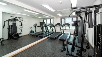 Un gimnasio con cintas de correr, máquinas de pesas y un espejo grande.