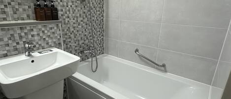Un baño con un lavamanos blanco, una bañera, una ducha y una pared de azulejos con un diseño en mosaico.