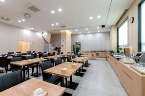 A spacious dining area with multiple tables and chairs, a kitchen counter with various appliances, and a large window providing natural light.