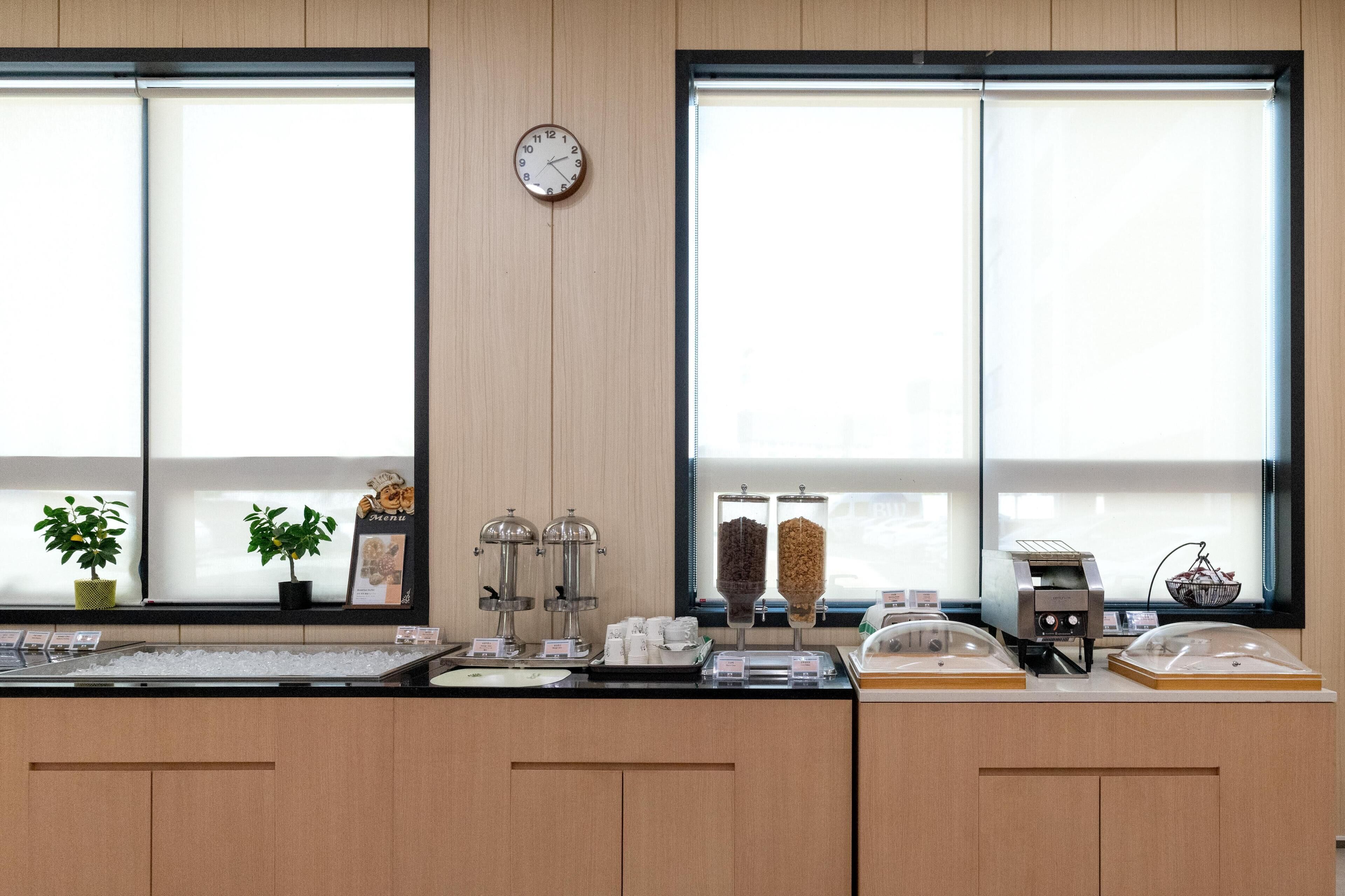 Un bar pour prendre le petit-déjeuner, avec une horloge, deux plantes en pot et une machine à café.
