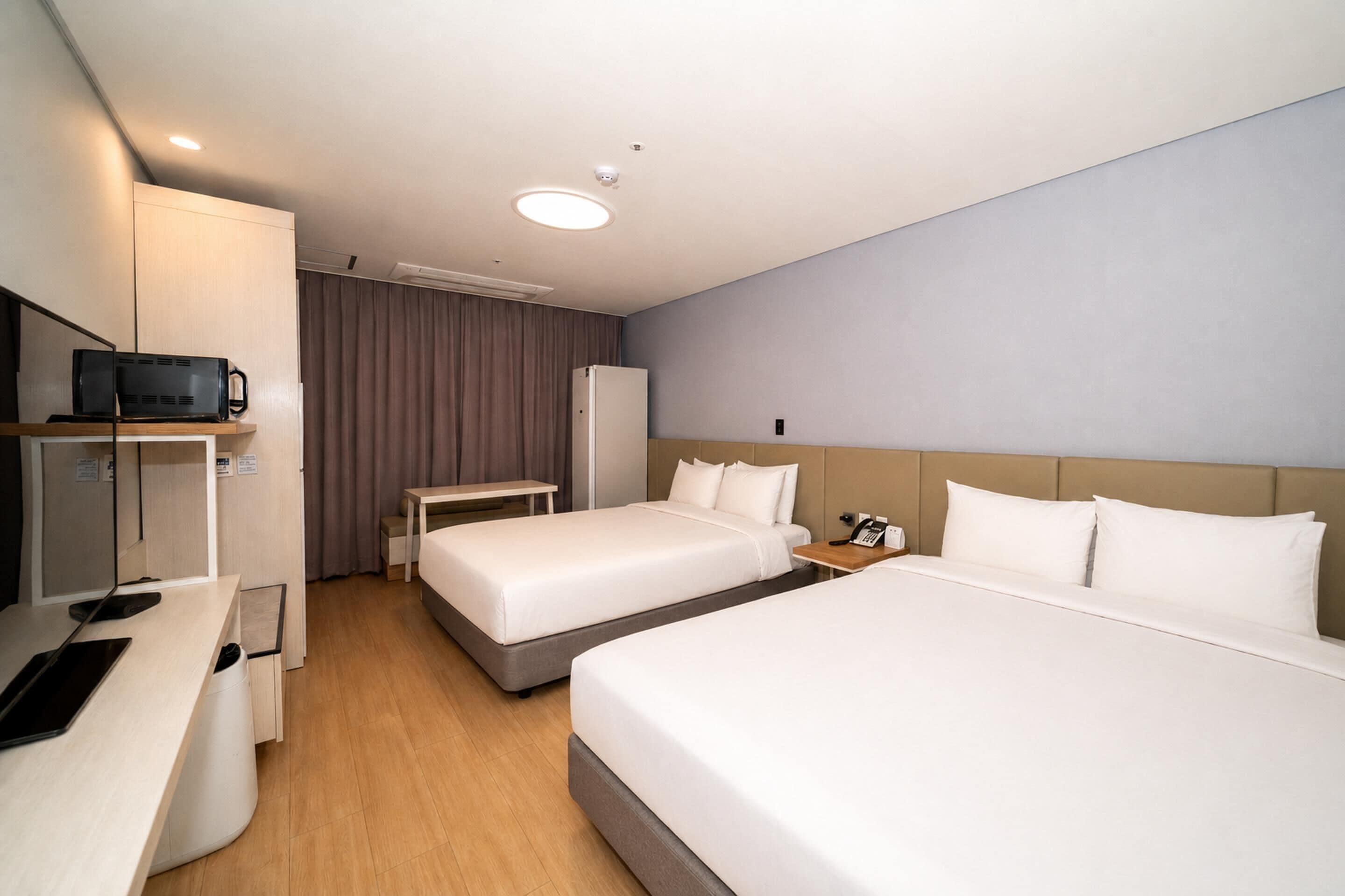 A hotel room with two beds, a desk, a television, and a refrigerator.