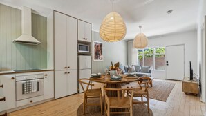 Une cuisine moderne avec des meubles blancs, un four encastré et un coin repas comprenant une table ronde en bois et des chaises.