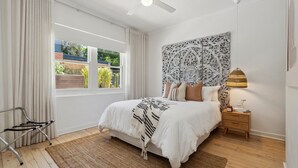 Une chambre à coucher comprenant un lit, une table de chevet, une lampe, un ventilateur de plafond et une fenêtre avec des rideaux.