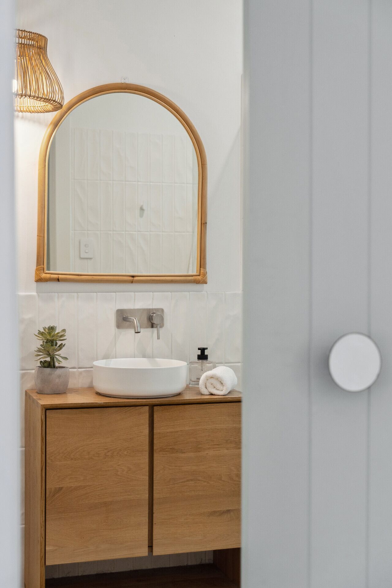 Een badkamer met een witte wastafel, een houten kastje, een spiegel met gouden lijst, een potplant en een handdoek op het aanrecht.
