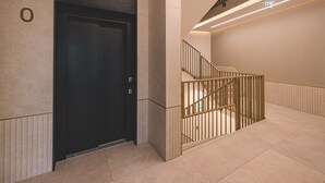 Un ascenseur moderne, un escalier doté de rampes métalliques et un aménagement intérieur épuré et minimaliste.