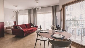 Un salon moderne avec un canapé rouge, une table à manger dressée pour deux personnes et une grande fenêtre équipée de stores.