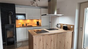 Une cuisine moderne dotée d’un îlot central, de meubles blancs, d’une cuisinière encastrée et d’une hotte en acier inoxydable.