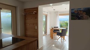 Une cuisine moderne avec des armoires en bois et une cuisinière intégrée. On y trouve un coin repas avec une table et des chaises, et une vue sur la verdure à l’extérieur.