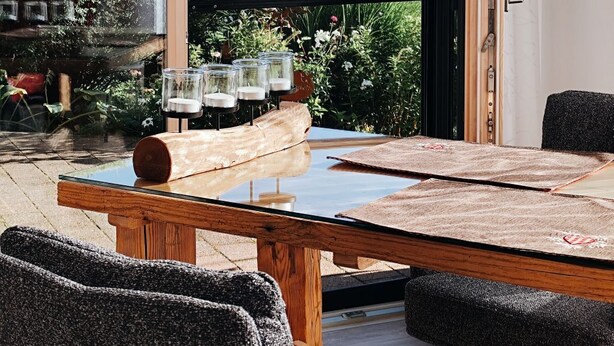 Un espace repas comprenant une table et des chaises, une vue sur la verdure et les montagnes grâce à de grandes fenêtres, et une porte coulissante.