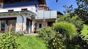 Une maison à deux étages dotée d’un balcon, entourée d’une végétation luxuriante et d’une pelouse bien entretenue.