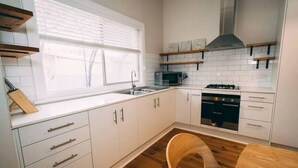 Moderni keittiö, jossa on valkoiset kaapit, ruostumattomasta teräksestä valmistettu liesi ja puinen ruokapöytä.