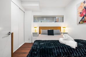 Un dormitorio con una cama, dos mesitas de noche, un cabecero, una ventana y un cuadro en la pared.