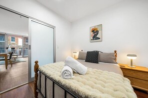 A bedroom with a bed, bedside tables, a nightstand, a painting, and a view of an outdoor balcony. - Tropicana on Bent—A Walkable Adelaide CBD Base (Adelaide)