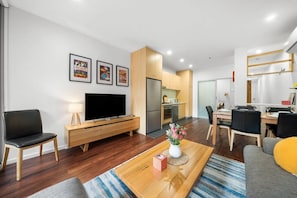 Una sala de estar moderna con un televisor de pantalla plana, una mesa de centro de madera y un comedor con mesa y sillas.