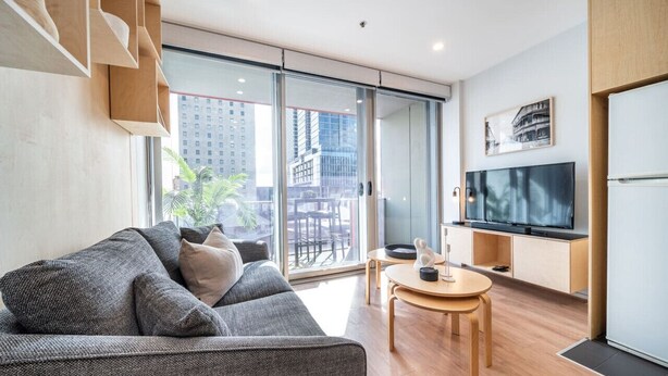A modern living room with a grey sofa, a wooden dining table, and a flat-screen TV. - Paradiso on Bent—City Chic near Rundle Mall (Adelaide)