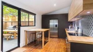 A modern kitchen with a wooden table, bar stools, a stainless steel refrigerator, and a view of the outdoors. - Blackbird at Arlo`s—Heritage meets Designer Charm (Glenelg South)