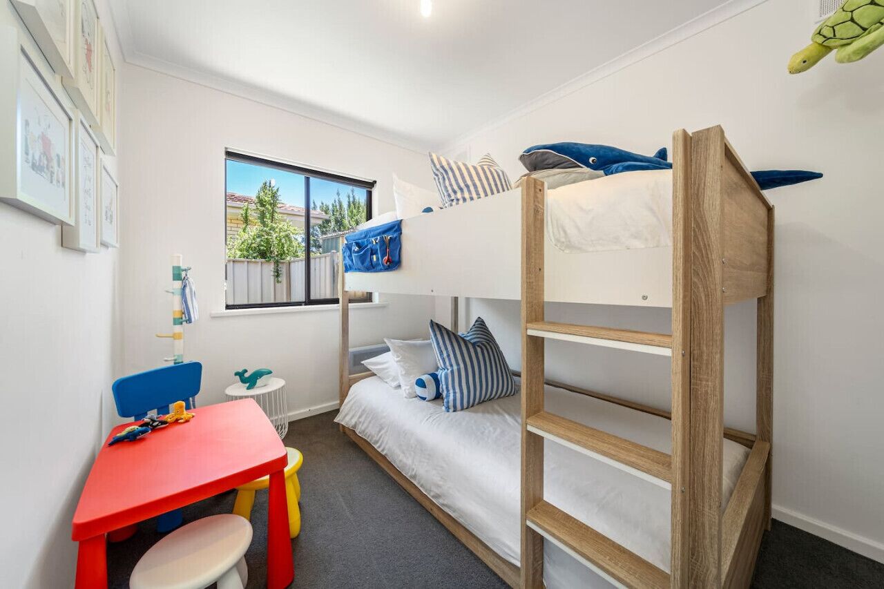 A bunk bed room with a desk and chair, a window with a view of greenery, and a turtle plush toy on the wall.
