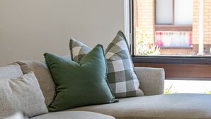 En stue med sofa, puder, et vindue og udsigt til en bygning.