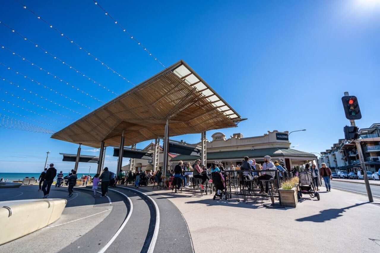 Un espace extérieur abrité avec des tables et des chaises, un ciel bleu dégagé et un bâtiment avec une enseigne visible à l’arrière-plan.