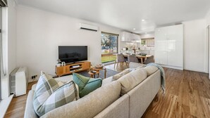 En moderne stue med sofa, fjernsyn og et spiseområde med stole og bord.