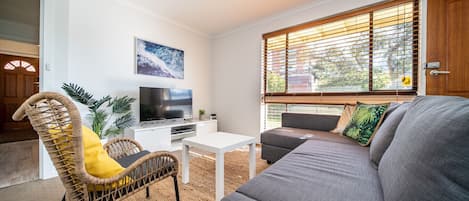 A living room with a sofa, a television, a white coffee table, and a wicker chair.