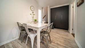 Un petit coin repas avec une table blanche et quatre chaises, une plante en pot et une horloge murale.