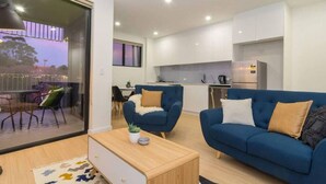 A modern apartment with a living room, dining area, and kitchen. There is a balcony with outdoor seating. - Canopy @ 44—Central CBD Location (Ovingham)