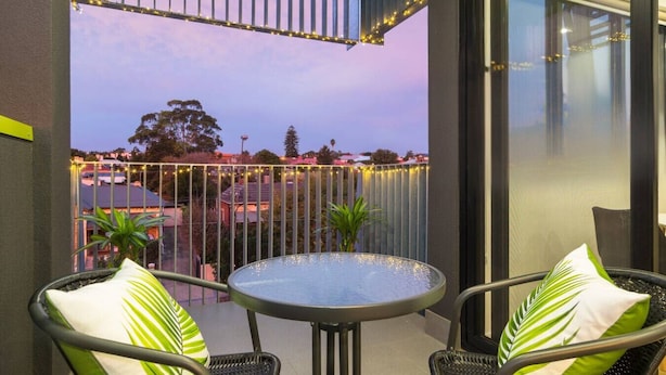 A balcony with a round table, two chairs, and a view of a residential area. - Canopy @ 44—Central CBD Location (Ovingham)