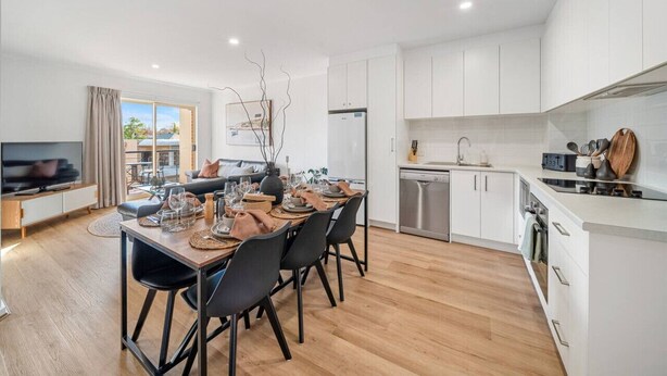 A modern kitchen with white cabinets, a dishwasher, and a dining area with a wooden table and chairs. - In The Midst on Melbourne - Walk to Cafés & Dining (North Adelaide)