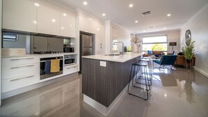 Cocina moderna con armarios blancos, una isla central y un área de comedor con sofá y taburetes de bar.