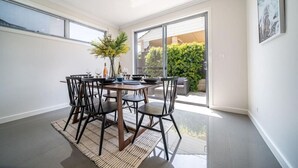 Comedor con una mesa dispuesta para cuatro personas, rodeada de sillas, y vistas a zonas verdes.