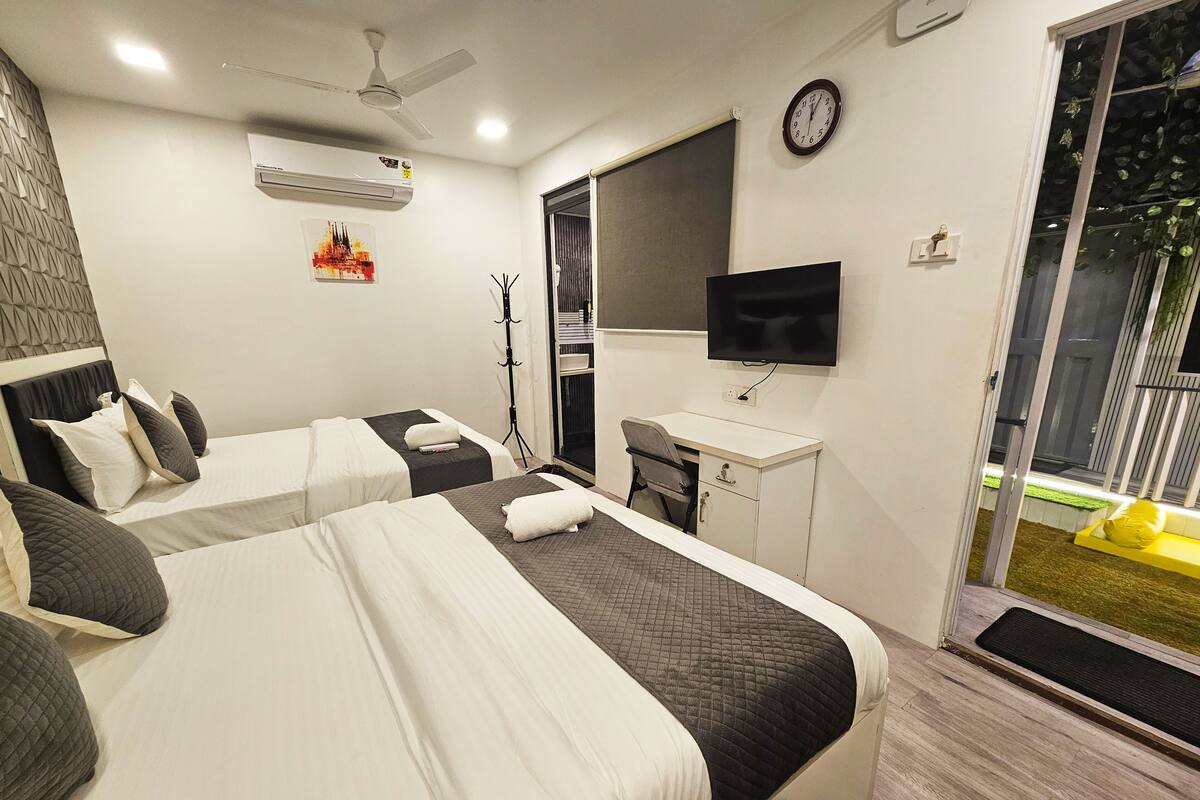 A hotel room with two beds, a desk, a TV, and a window with a view of the outside.
