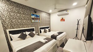 A hotel room with two beds, a desk, a wardrobe, a wall clock, and a mounted picture. - Astha Home Shared Pool Rooms (Mumbai)