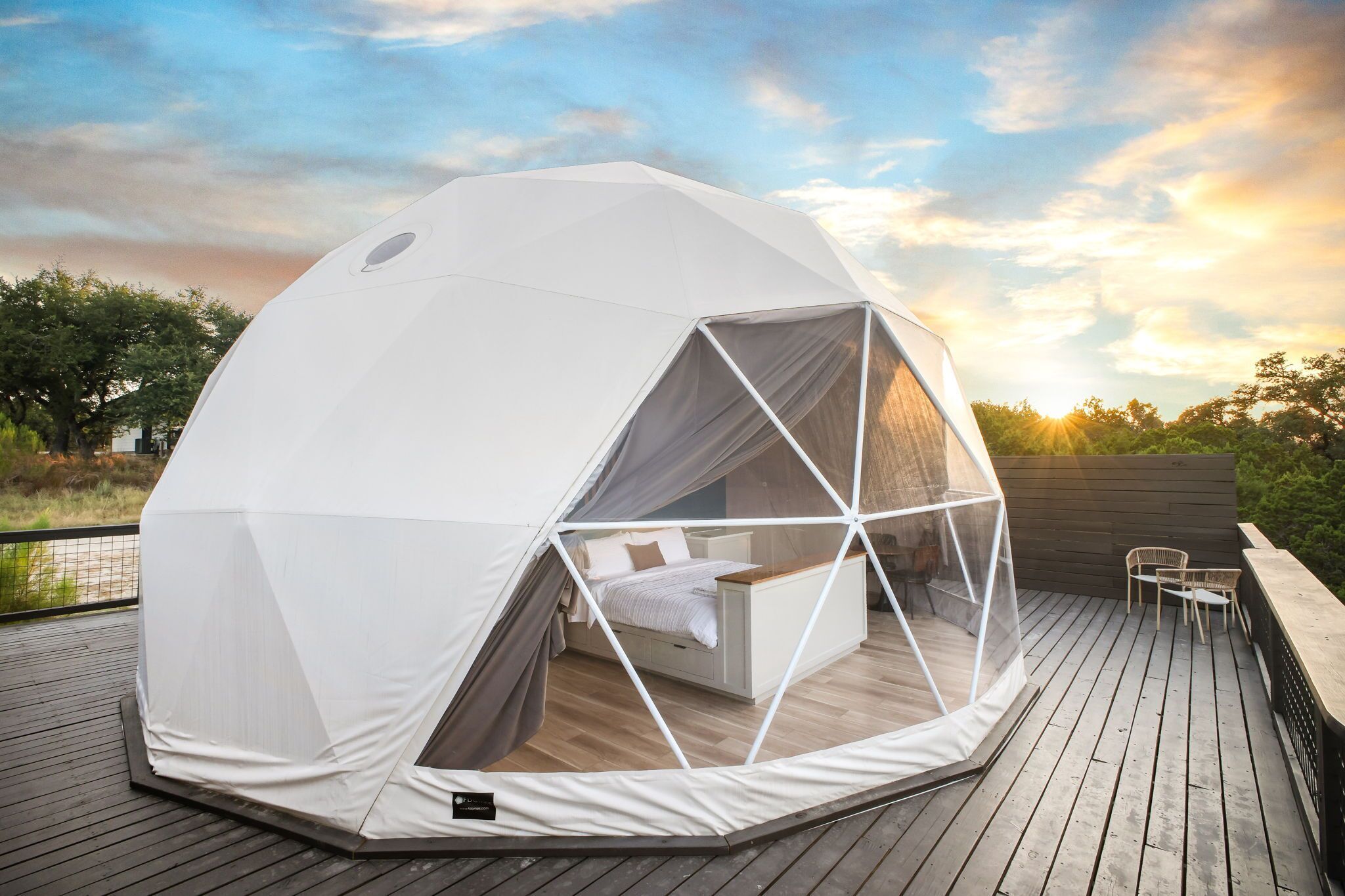 Une tente en forme de dôme géodésique, dotée d’un lit et d’un espace salon sur une terrasse en bois.