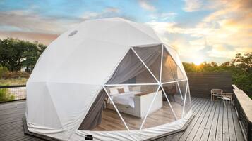 Une tente en forme de dôme géodésique, dotée d’un lit et d’un espace salon sur une terrasse en bois.
