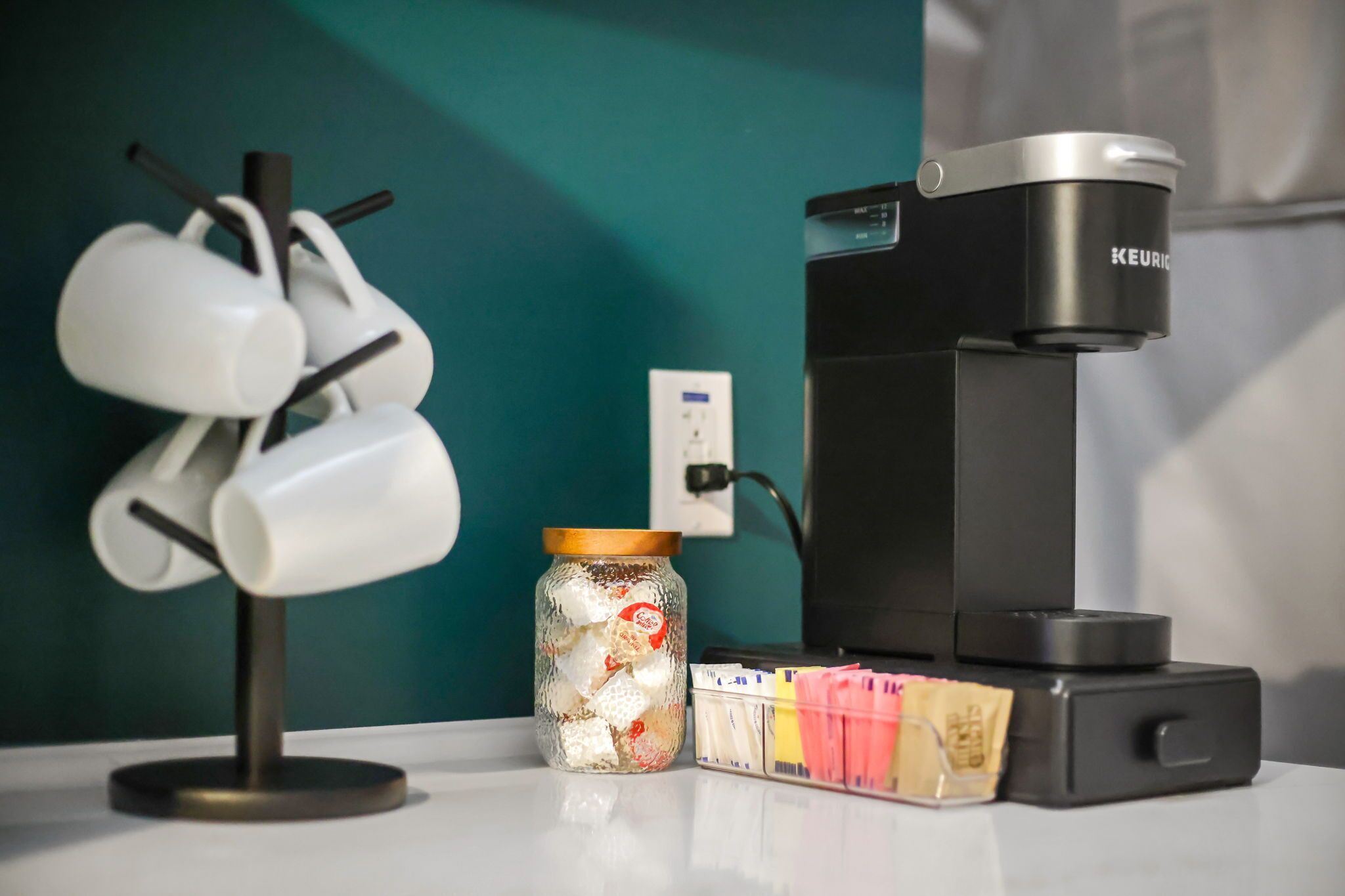 A coffee machine, a jar with white cubes, and a mug holder on a counter.