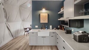 A modern kitchen with a white countertop, a sink, and a microwave. There is a small table with chairs and a vase of flowers on the wall. - Luxury Dome - Spa Shower - Panoramic Views (Spring Branch)