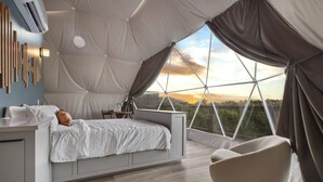 A bedroom with a bed, a chair, and a view of the sunset through large windows. - Luxury Dome - Spa Shower - Panoramic Views (Spring Branch)