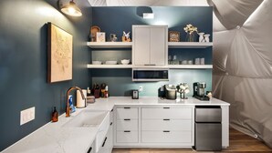 A modern kitchen with white cabinetry, a microwave, and a built-in oven. There are shelves with decorative items and a sink with a faucet. - Luxury Dome - Spa Shower - Panoramic Views (Spring Branch)