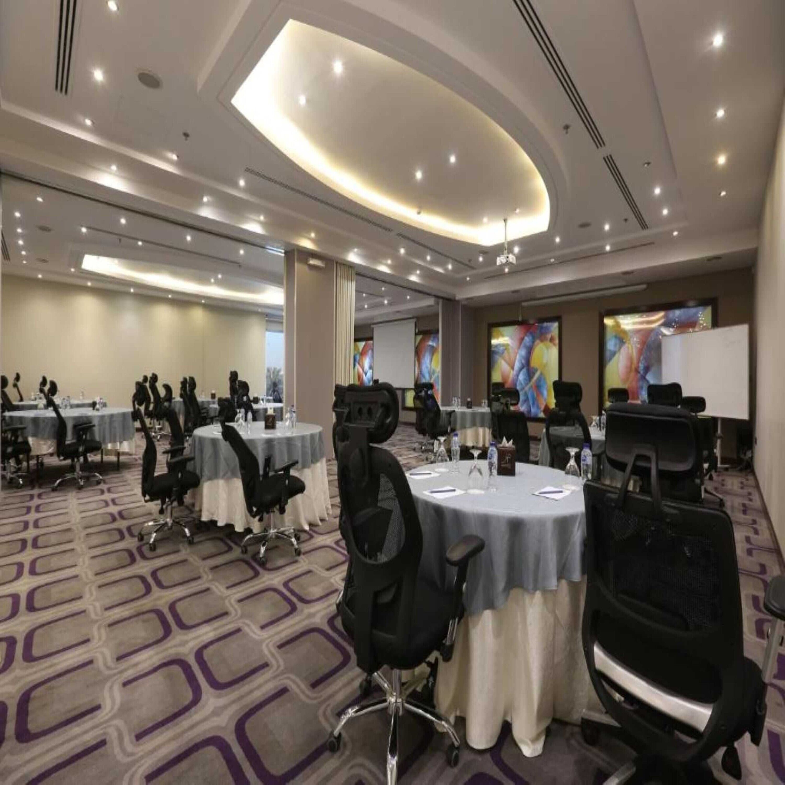 A conference room with round tables, chairs, and a presentation screen.